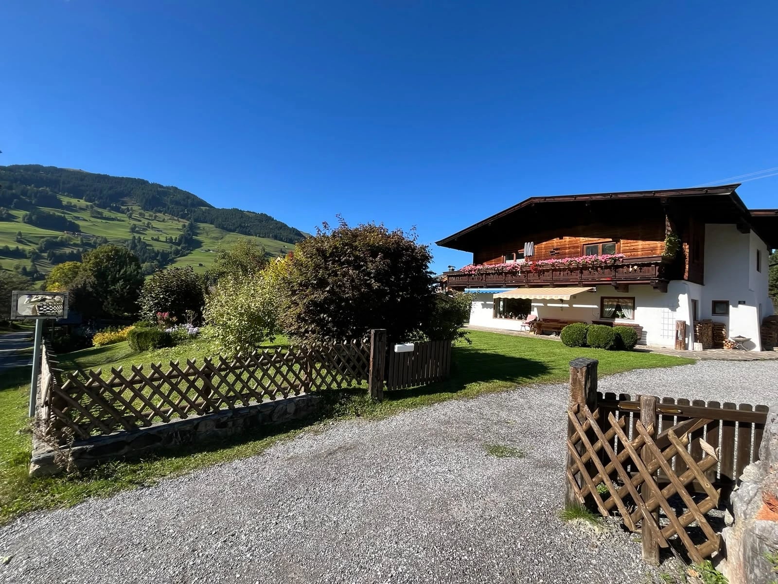 Das bestehende Haus am Grüntalweg 12 mit blühendem Holzbalkon, Garten und Bergblick